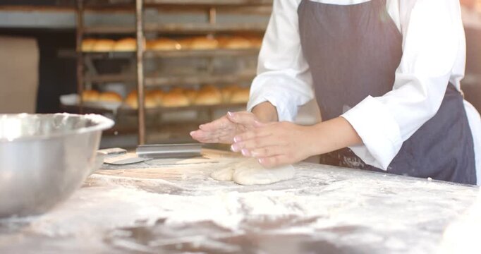 African-American woman in white chef-shirt and dark-apron pressing folding and shaping dough to ba