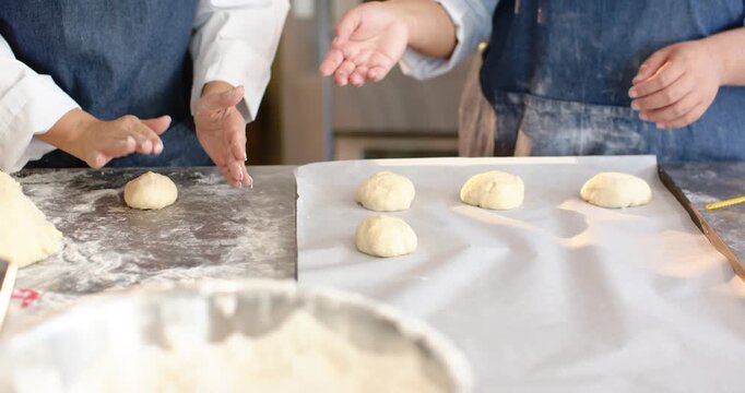 2 women bakers responding to portioned dough shaping and placing six balls on parchment for baking