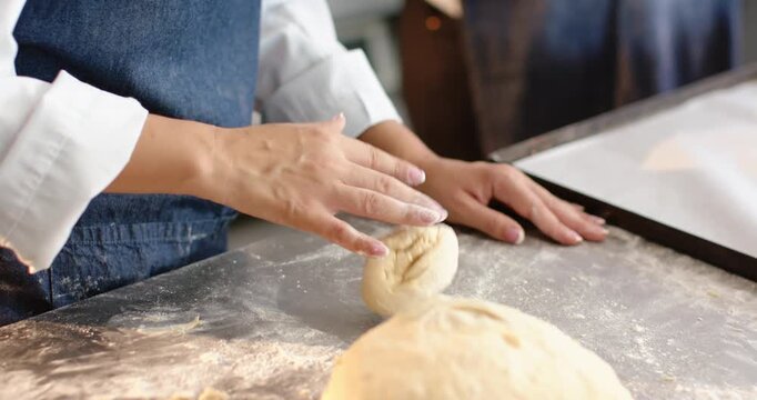 African American woman in apron cutting proofed dough shaping buns for baking at floured table