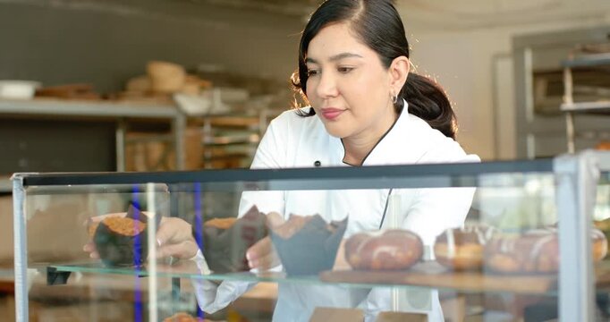 Noticing misaligned muffins, pastry chef is aligning muffins and rolls on glass shelves for display