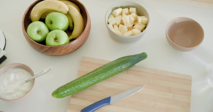 Top-down camera panning right, revealing cucumber on kitchen cutting board with knife for blending