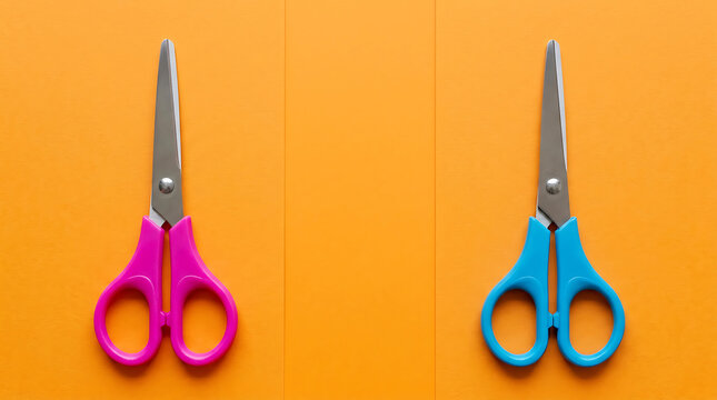 Pair of pink and blue scissors placed vertically on bright orange background for school craft and creativity