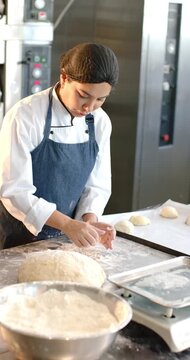 Diverse female coworkers dusting flour, kneading and shaping bulk dough at prep table for baking