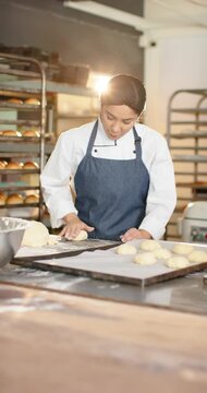 Female baker placing dough cutting with scraper, rolling onto tray for baking at bakery chef-jacket