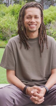 African American man sitting on bench in garden, smiling then laughing, showing bracelets