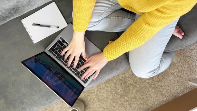 This video footage showcases a person typing on a laptop while seated comfortably. A notebook is placed nearby, creating a cozy workspace atmosphere. Ideal for educational or lifestyle projects.