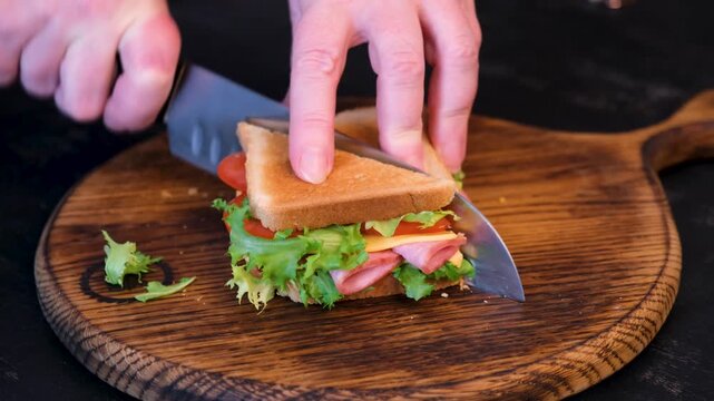 Cutting sandwich with knife revealing layers of ham cheese and vegetables