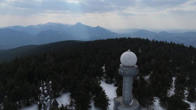 Aerial view of a weather radar station and communication towers on a snowy mountain peak at spring