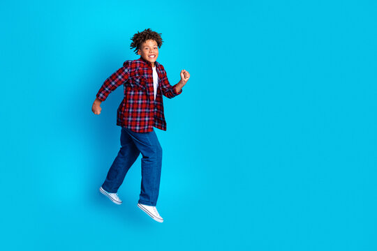 Happy boy jumping against bright blue background wearing plaid shirt, jeans and sneakers, energetic carefree child portrait