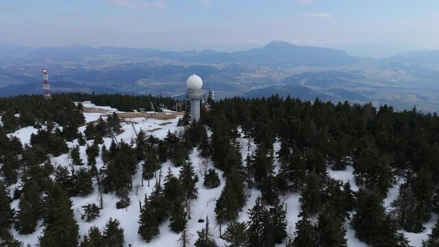 Aerial view of a weather radar station and communication towers on a snowy mountain peak at spring