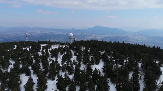 Aerial view of a weather radar station and communication towers on a snowy mountain peak at spring