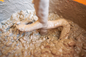 Fototapeta premium Close up of an electric paddle mixing heavy textured concrete with aggregate stones in bucket showing texture and construction material detail. Heavy duty building industrial work