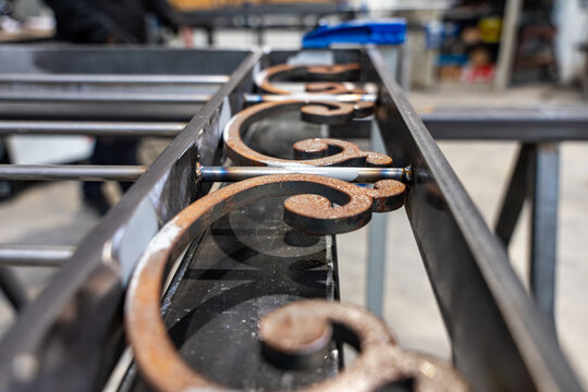 D&eacute;tail de volutes en fer forg&eacute; avec points de soudure sur un cadre m&eacute;tallique dans un atelier de ferronnerie d'art.