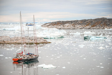 Ilulissat, Disko Bay, Greenland - Two Sailboats Rafted Together, Icebergs Drifting by under a sunset in Iceberg Alley along a rugged Greenlandic coastal landscape in Ilulissat Icefjord. © SJ Falcetta Images