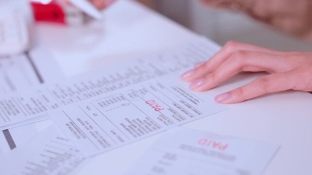 Professional hand applying red rubber stamp to business paperwork during focused finance accounting reviewing process showing diligent effort analyzing paid invoice document at white office desk