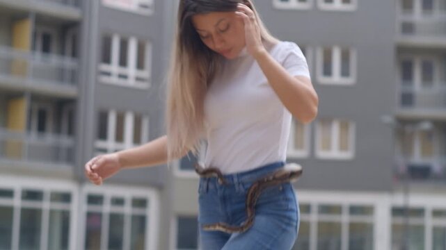 Young woman holding python snake around her waist in abandoned urban environment, wild animal concept