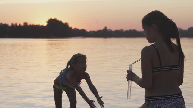 Funny girl catches bubbles on the shore of the lake, which her older sister lets go