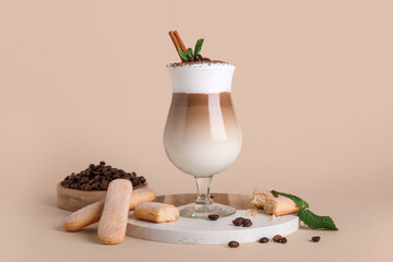 Naklejka premium Glass of tasty Tiramisu cocktail with coffee beans, savoiardi, cinnamon stick and mint leaves on beige background