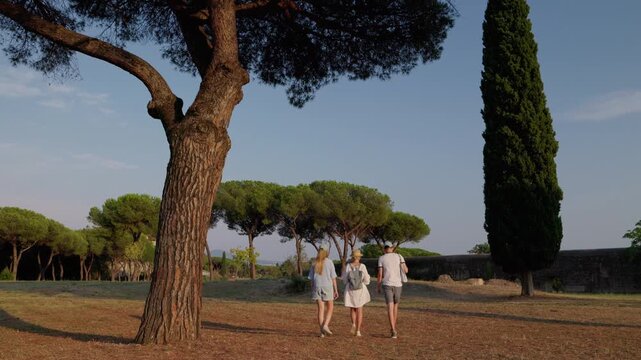 Family walking in Appia Antica Park Rome under pine trees with ancient aqueduct and warm evening light