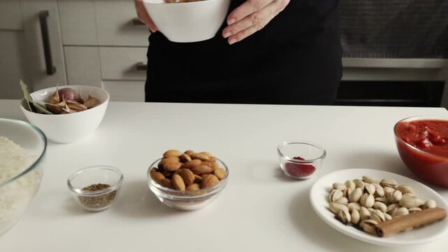 close-up of hands presenting a white bowl of golden raisins near almonds pistachios garlic and tomato mixture, highlighting sweet and savory additions for an aromatic rice meal