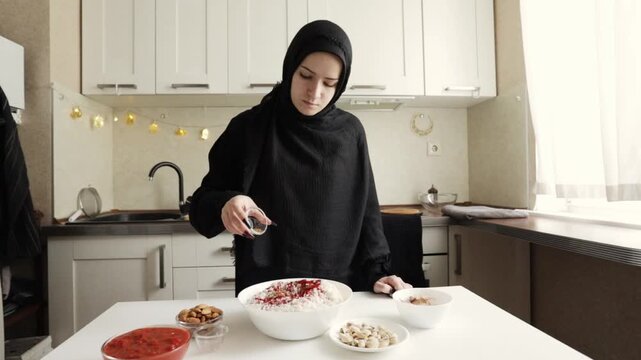 muslim woman in black hijab adds a spice blend into a large white bowl of uncooked basmati rice, preparing the base for a fragrant savory main course