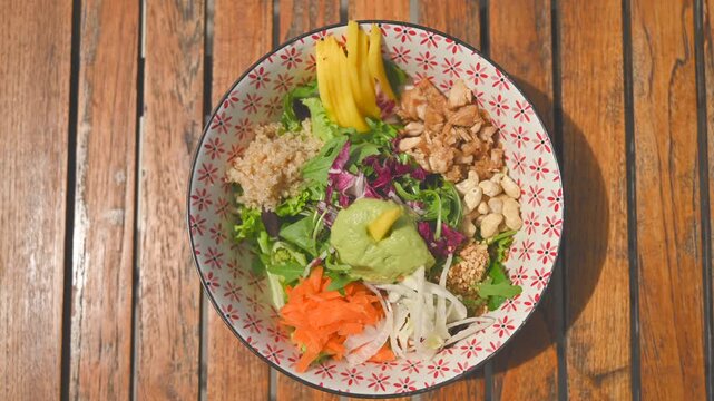 fresh summer salad bowl being placed on a wooden table. Colorful vegetables and natural ingredients create a healthy and appetizing scene, ideal for concepts related to nutrition