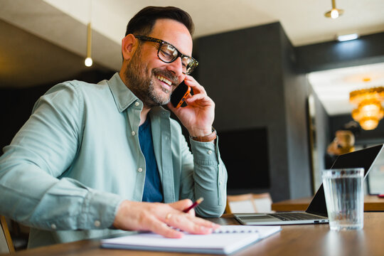Happy businessman talking on phone while working remotely in cafe