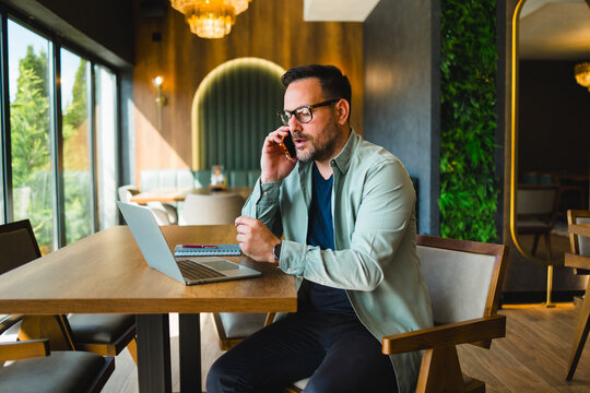 Man talking on smartphone while working remotely in cafe