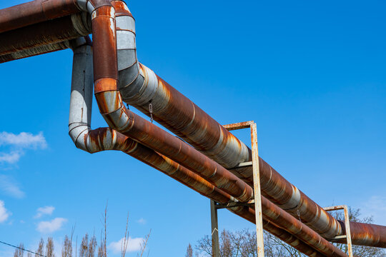 Old rusty industrial heating pipes against clear blue sky, overhead district heating network, energy infrastructure and technical metal pipeline, steel tubes for resource transport in sunlight.