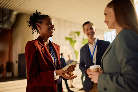 Happy black entrepreneur communicating with her coworkers while waiting for business seminar to start.