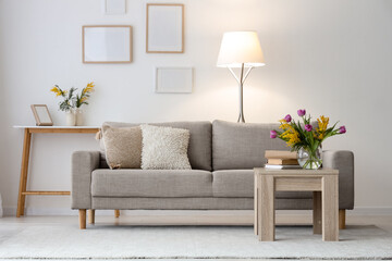 Interior of light living room with sofa, tables and spring flowers in vases
