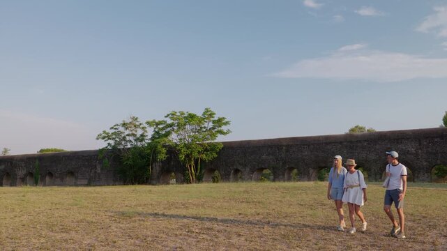 Family walking near ancient aqueduct in Appia Antica Park Rome during warm summer sunset with open landscape