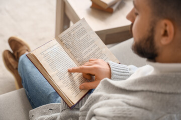 Naklejka premium Young man reading book on grey sofa at home, closeup