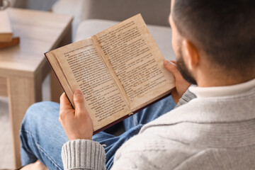 Naklejka premium Young man reading book on grey sofa at home, closeup