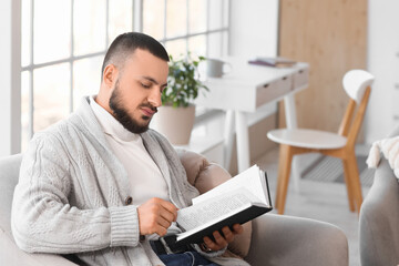Obraz premium Handsome young man reading book on armchair at home