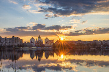 Golden sunset melts over Obolon embankment in Kyiv, painting the Dnipro River with shimmering reflections. Clouds drift softly as glowing domes and skyline dissolve into a calm, dreamy evening. © elena_suvorova