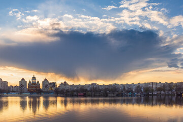 Golden sunset melts over Obolon embankment in Kyiv, painting the Dnipro River with shimmering reflections. Clouds drift softly as glowing domes and skyline dissolve into a calm, dreamy evening. © elena_suvorova
