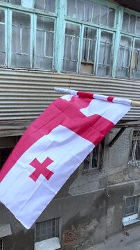 Vertical street video. 60 fps. Red white Georgian flag with cross on pole on balcony. Independence Day of Georgia. 26 may. Concept of patriotism, state, tourism, protest, fatherland, freedom, liberty