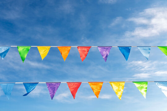 Rows of colorful pennant flags outdoors in realistic style on wispy clouds sky background, conveying cheerful celebration mood
