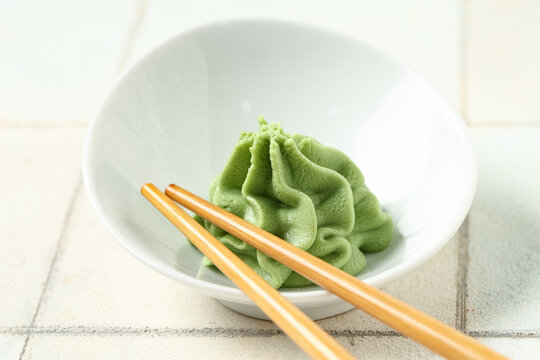 Bowl with wasabi paste and chopsticks on white tile background, closeup