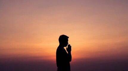 Fototapeta premium Silhouette of a man praying and meditating against a beautiful sunset sky background, concept of spirituality, faith, hope, and inner peace during a tranquil evening or morning sunrise.