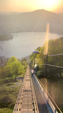 Funicular ascending through tunnel to Brunate overlooking Lake Como at sunset, scenic railway journey with dramatic exit revealing city skyline, mountains and glowing Italian landscape