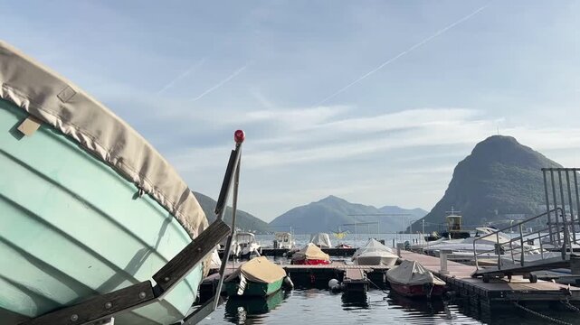 Time lapse of boats at small pier in Lake Lugano with Monte San Salvatore in the background, scenic harbor activity in Switzerland with mountain landscape