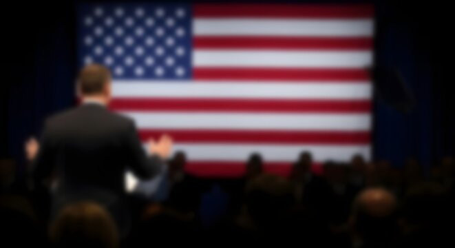 A blurred image of a person speaking in front of a large american flag symbolizing patriotism and national pride