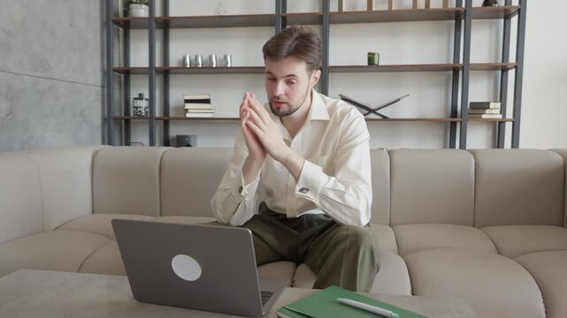 Worried Man Thinking And Looking At Laptop While Sitting On Sofa At Home
