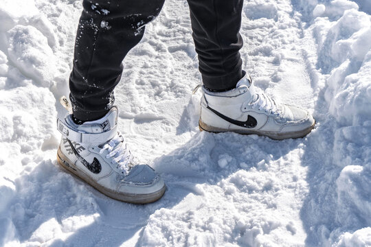 Sharkan, Russia - March 06 2022: Person stands on snowy surface wearing Nike Air Force 1 high sneakers. Snow is bright and covers ground in clear winter weather
