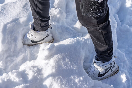 Sharkan, Russia - March 06 2022: Person stands on snowy surface wearing Nike Air Force 1 high sneakers. Snow is bright and covers ground in clear winter weather