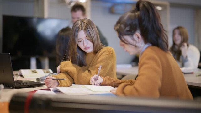 Students are engaged in a study session, discussing material and taking notes at a desk.