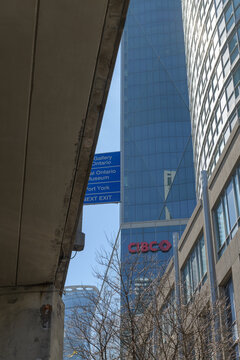 undercroft of the elevated Gardiner Expressway, blue signs, and facade of CIBC Square viewed from Lake Shore Blvd W at Yonge St, Toronto