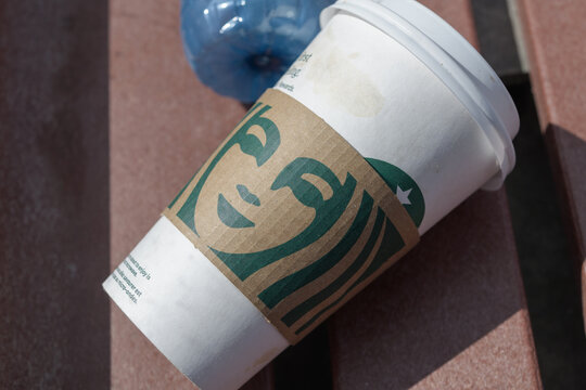 discarded Starbucks Coffee cup with cardboard zarf printed with a mythological Siren on a bus shelter bench, Toronto